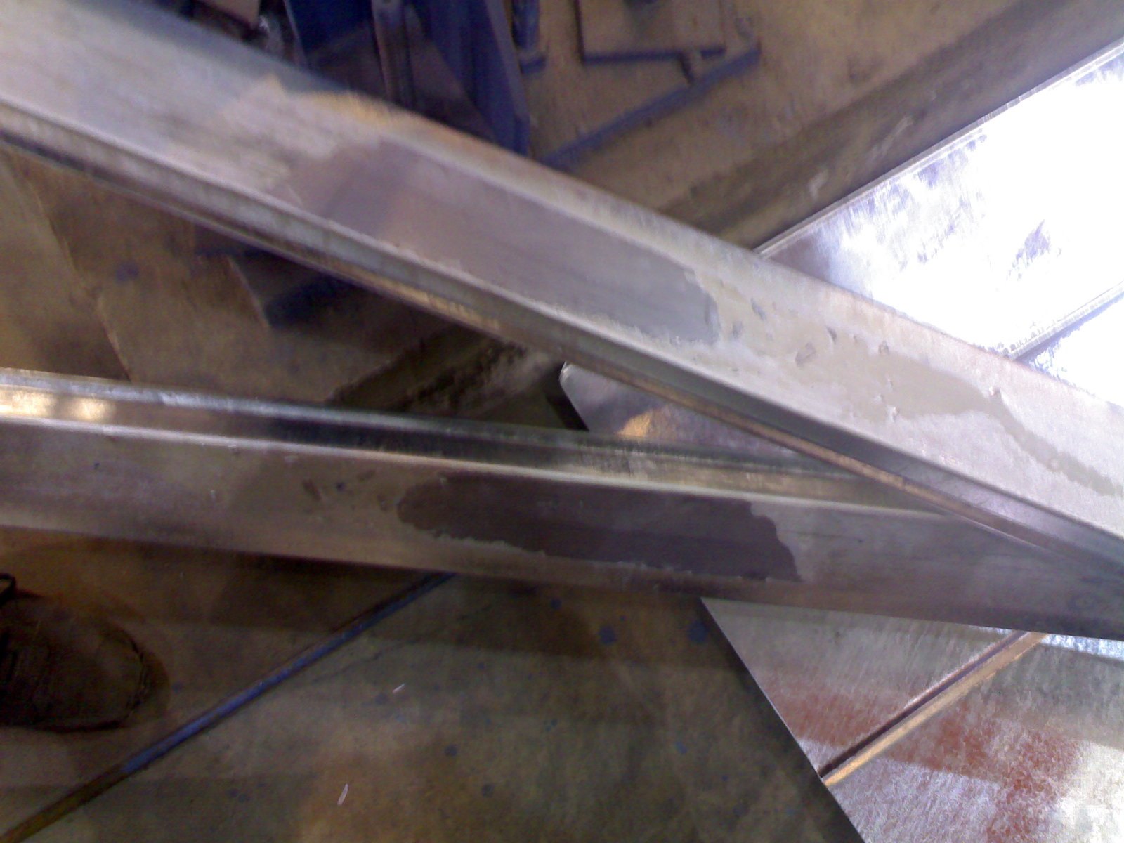 Two galvanized steel sections photographed after being separated: each carries a dull grey contact patch with straight edges where the pieces were stuck together in the zinc bath, against otherwise bright coating