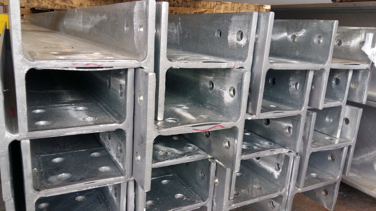 Stacked galvanized brackets, an open slot running along the plate-to-section joint on the nearest two, each traced with a red marker line