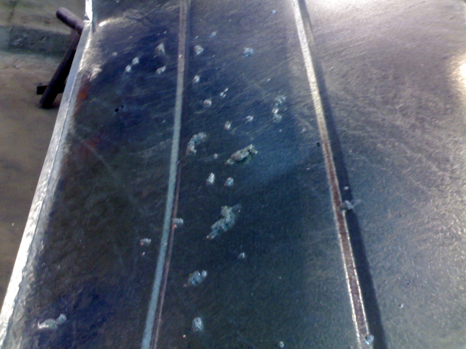Close-up of a galvanized beam surface scattered with small raised dross pimples in the zinc coating