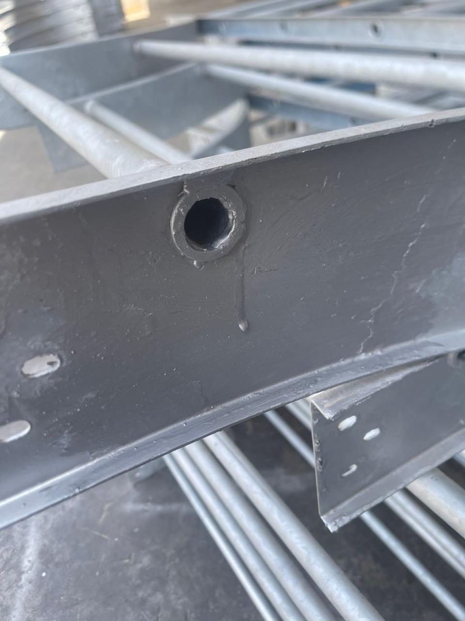 Galvanized bracket with a grey-green zinc-rich paint repair applied around a drilled hole, with a paint run visible below it