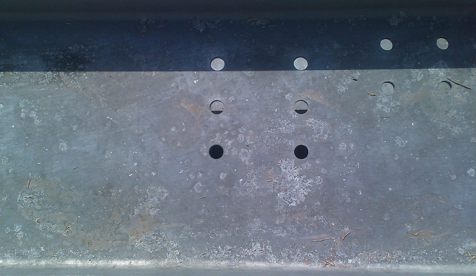 Galvanized channel section with white powdery wet-storage stain deposits spread across the face around drilled holes